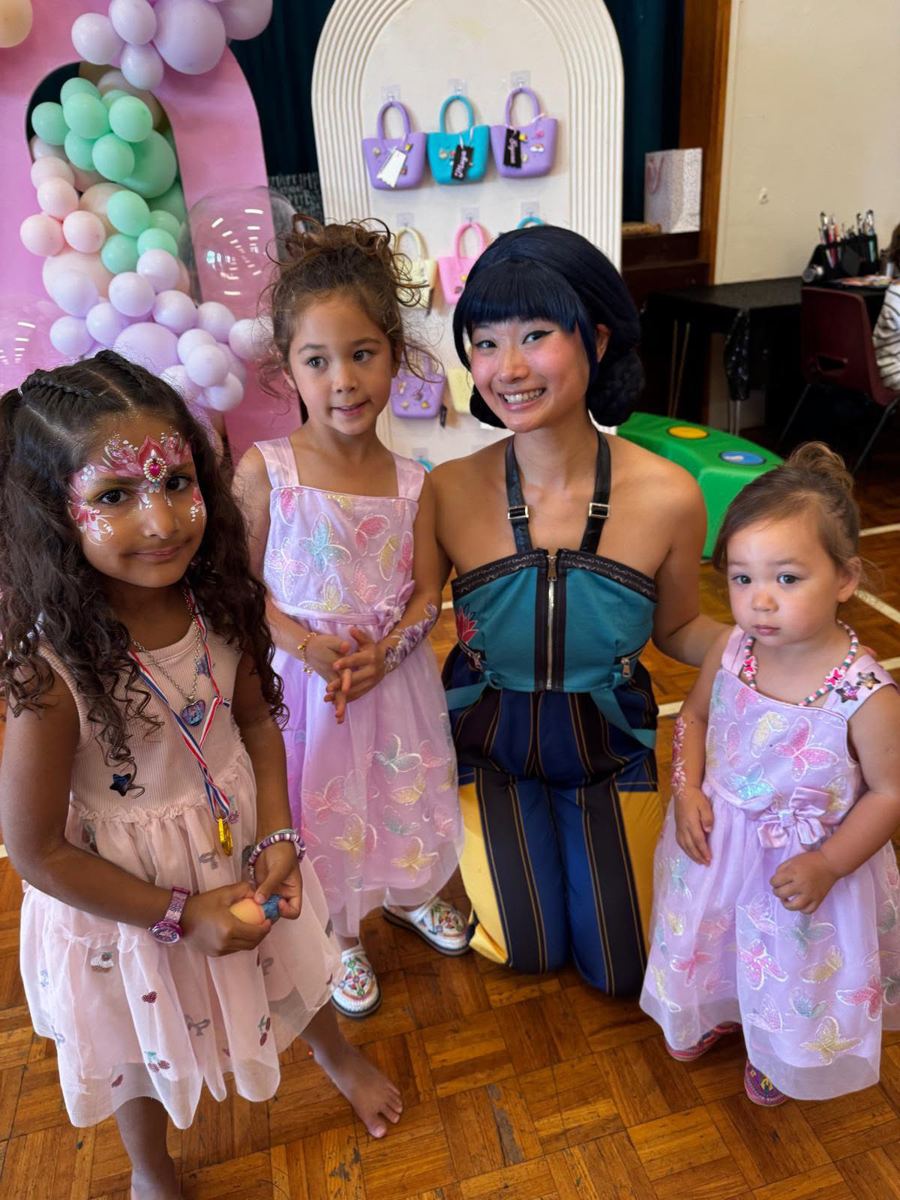 Performer with three girls in party dresses at a balloon-decorated hall