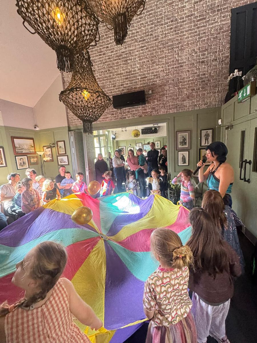 Children playing parachute games while the performer leads with a microphone