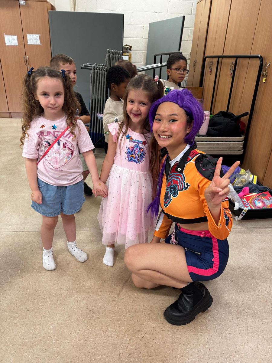 Performer in a purple wig and orange jacket with two smiling girls