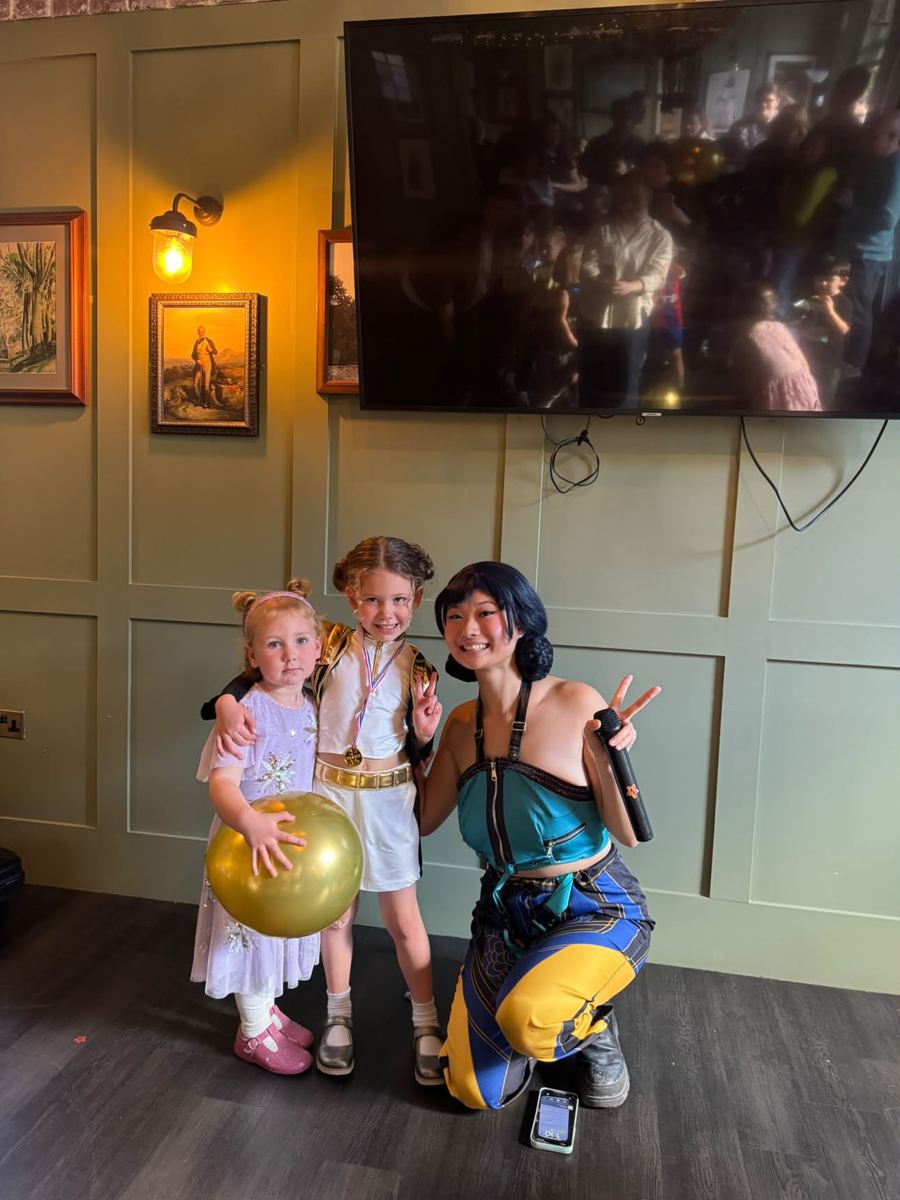 Performer holding a microphone with two young guests and a gold balloon