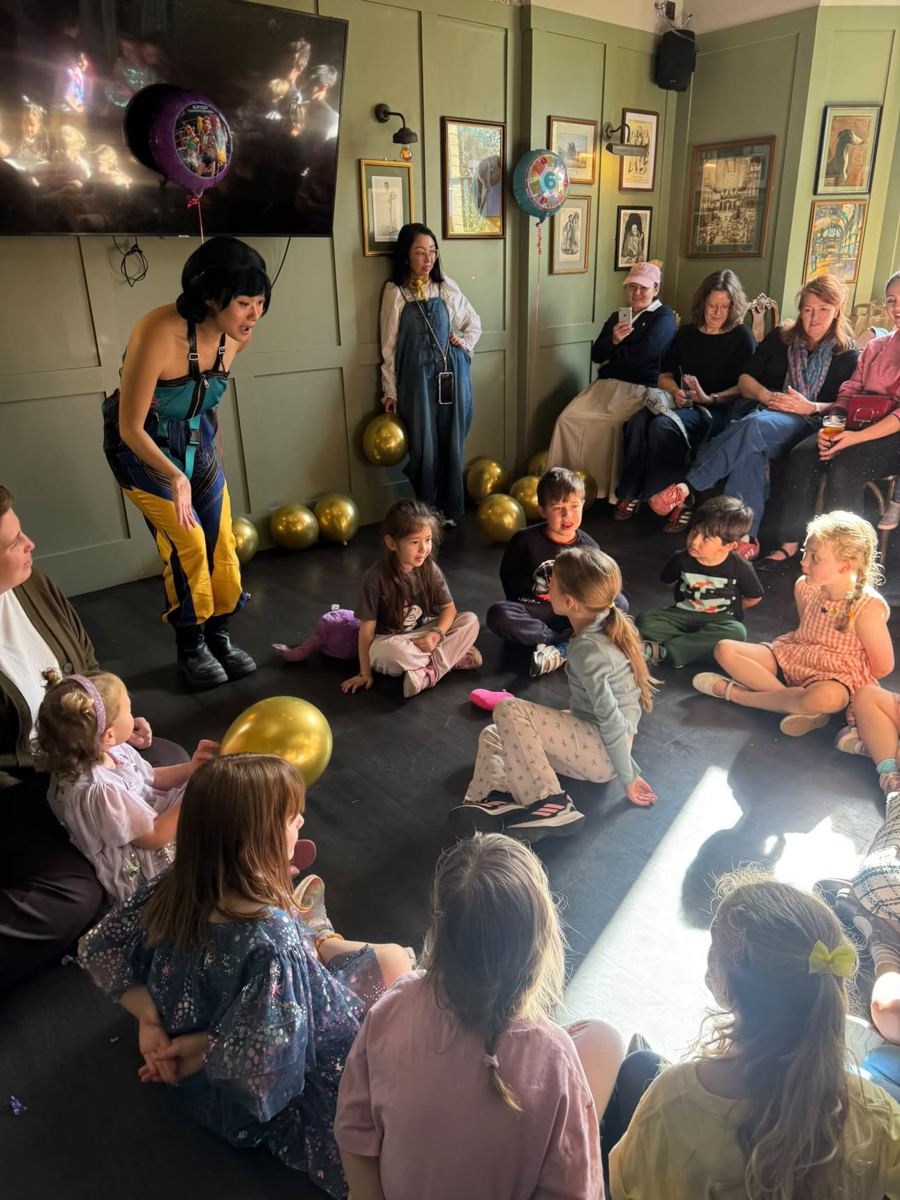Children cheering with their arms up around the performer in a pub party room